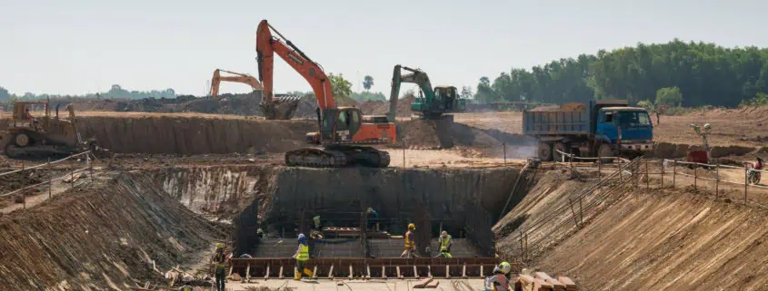 Baustelle mit Bauarbeitern, Baggern und Krandiensten bei Tiefbauarbeiten, Sicherungsmaßnahmen im Einsatz.